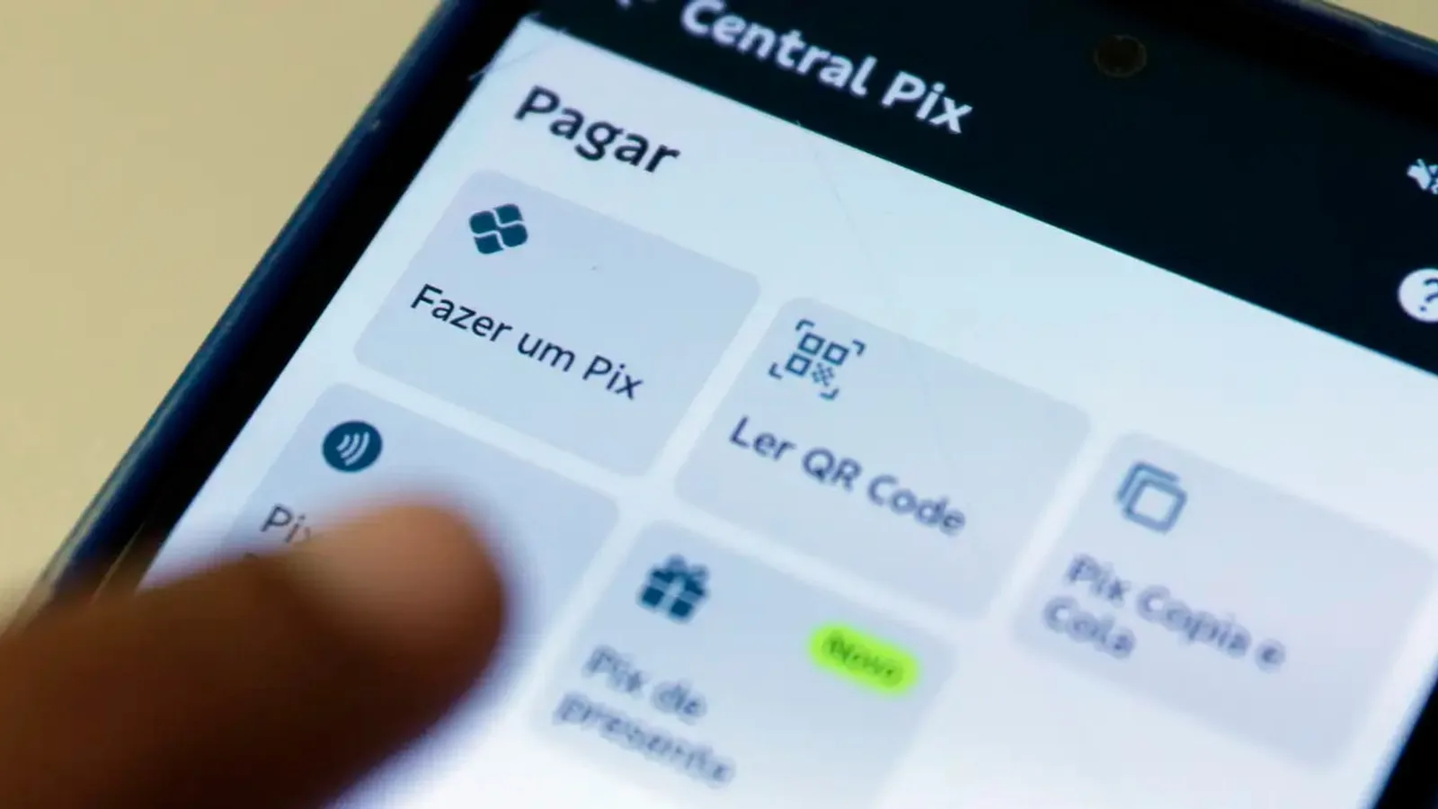 Dedo tocando a área Pix de um aplicativo de banco no celular, com as opções Fazer um Pix e Ler QR Code
