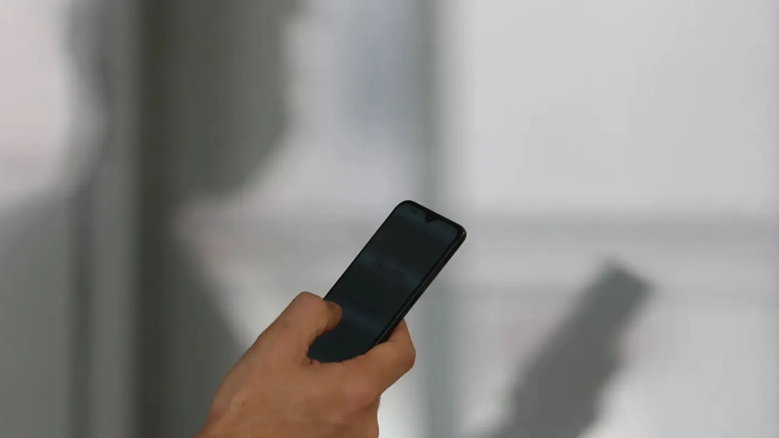 Mão segurando um celular, com a sombra da pessoa projetada na parede ao fundo