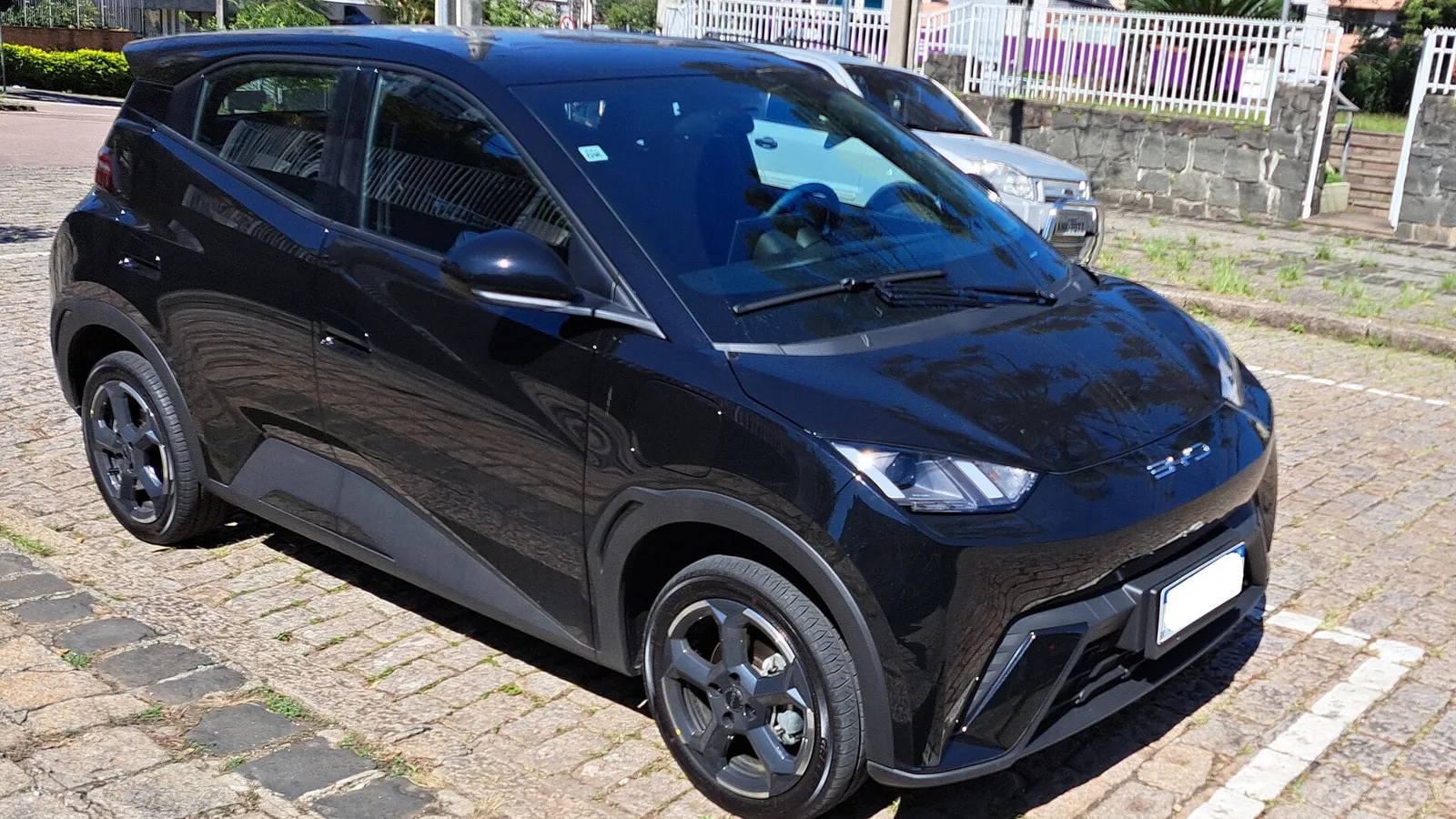 BYD Dolphin Mini preto, hatch elétrico compacto, estacionado em rua de paralelepípedos