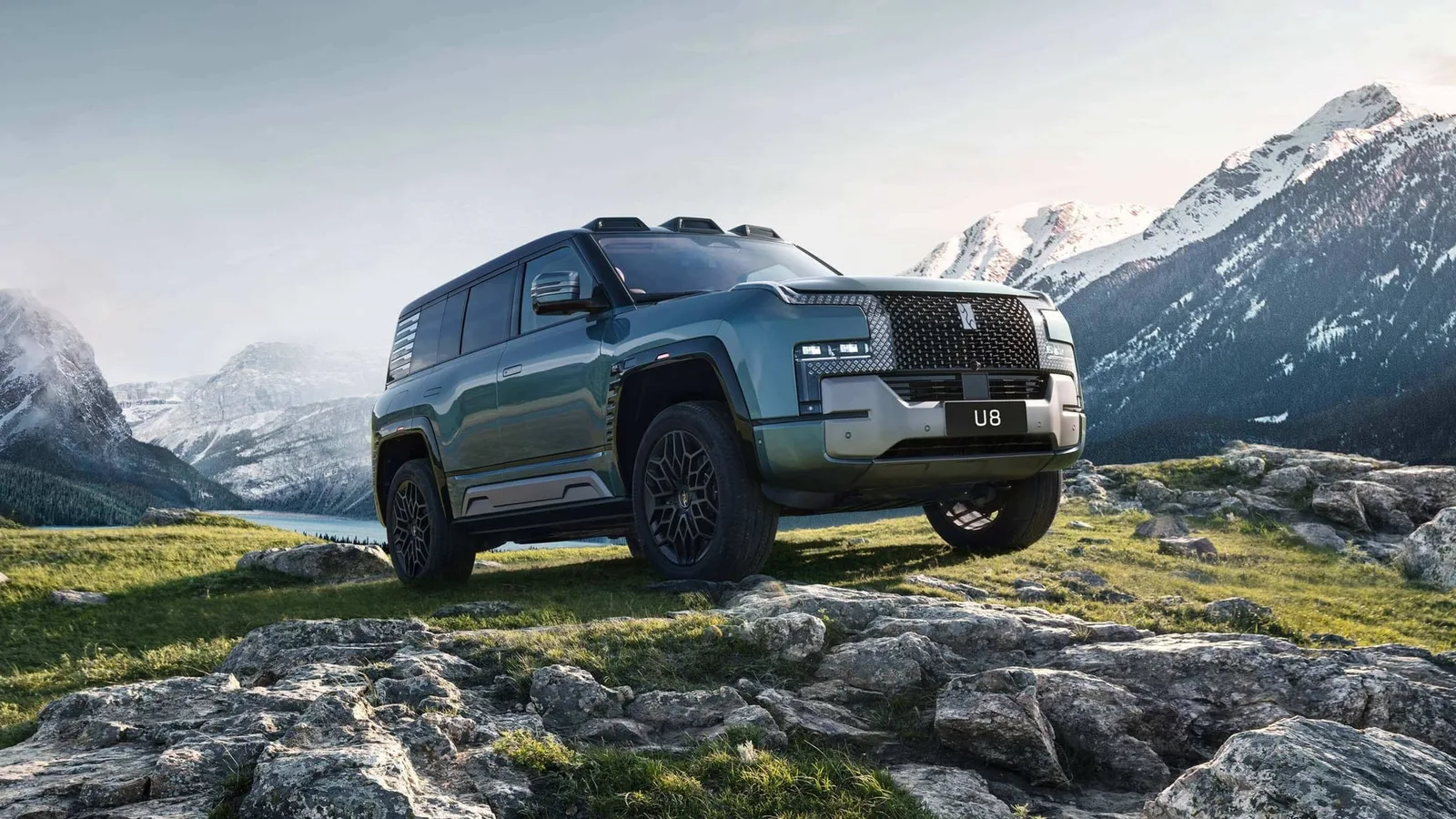 SUV Yangwang U8 verde parado sobre pedras em uma paisagem de montanhas nevadas