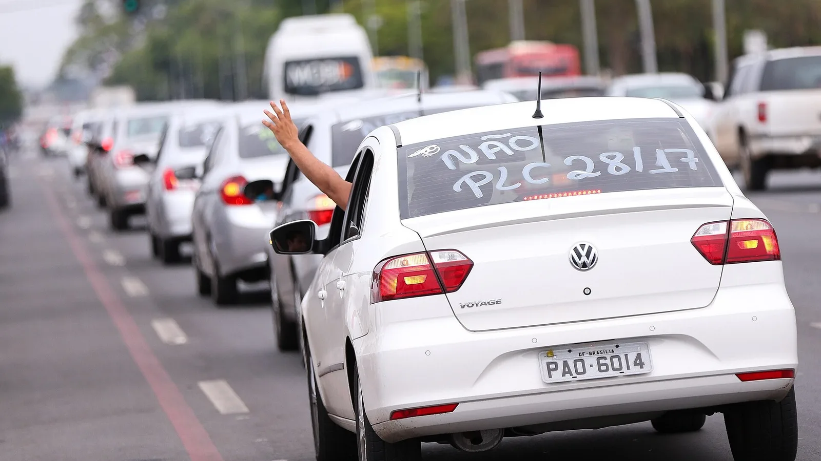 Sedan branco Volkswagen Voyage em fila de carros de motoristas de aplicativo em Brasília, com a mão do motorista para fora da janela