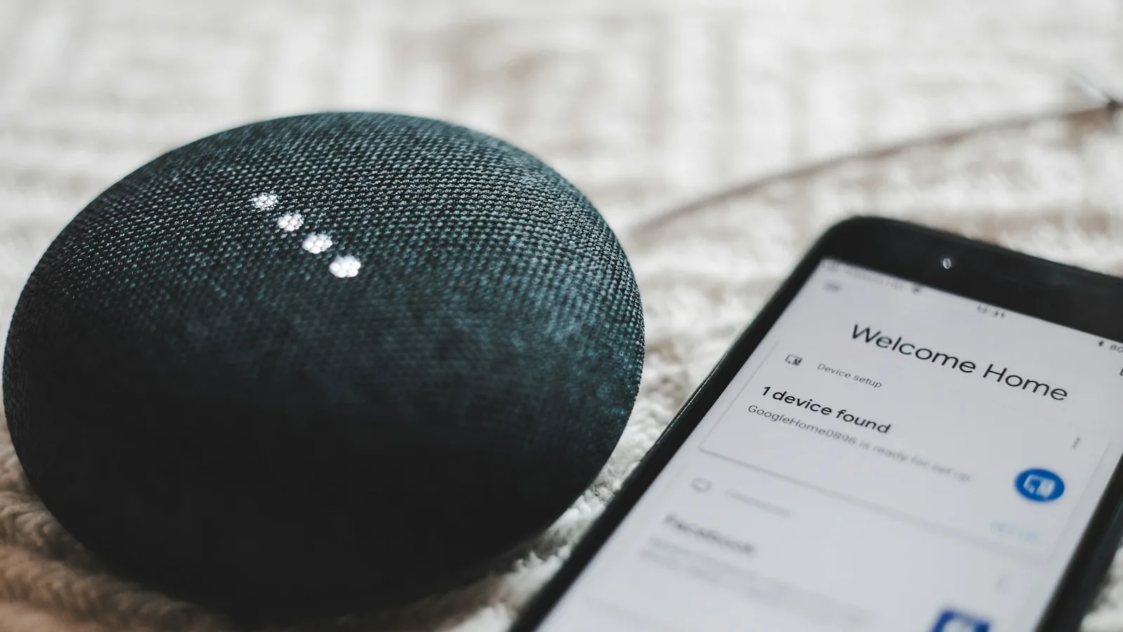 Alto-falante inteligente Google Home Mini ao lado de um smartphone com o app de configuração aberto