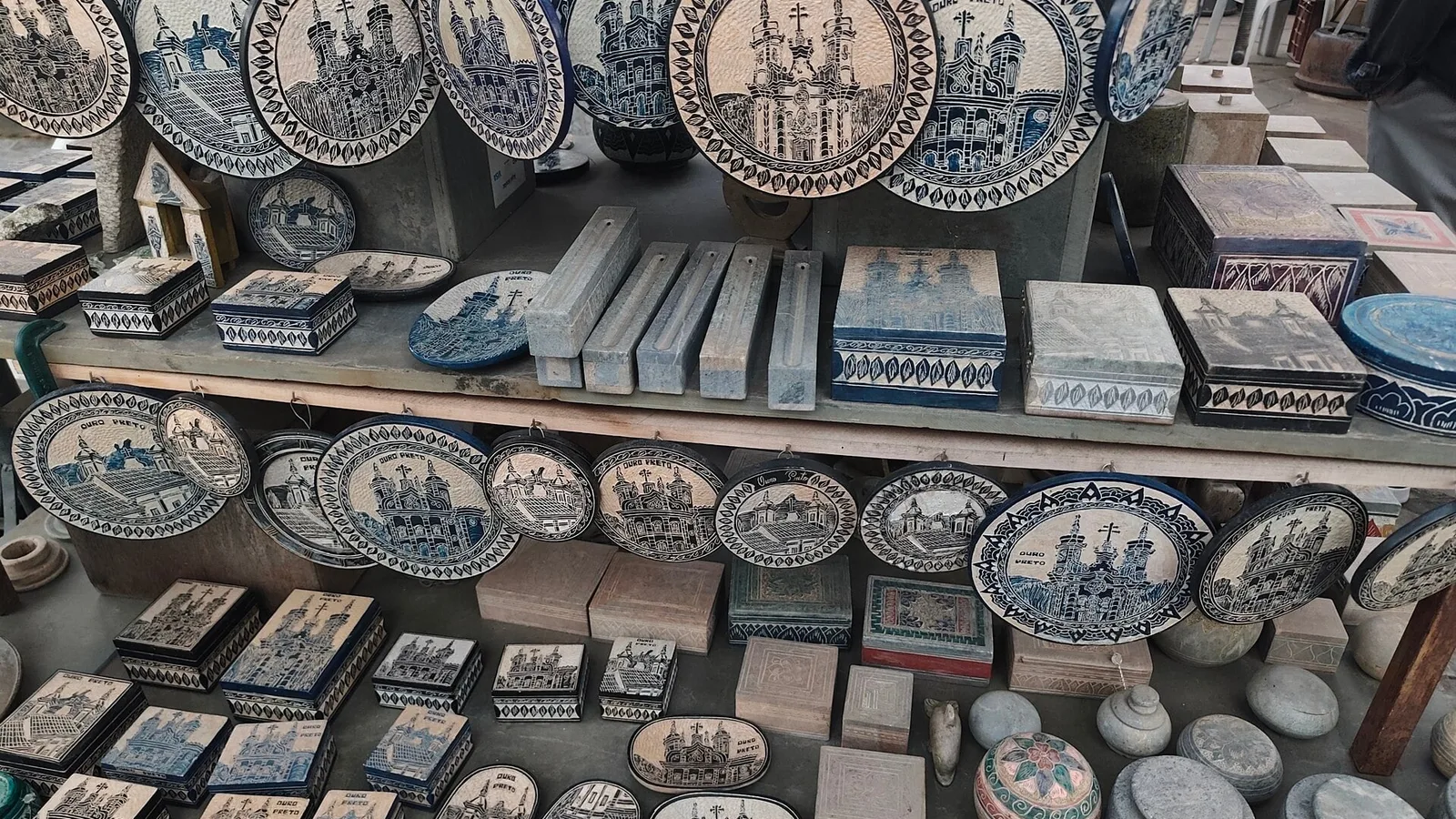 Artesanato de pedra-sabão exposto em prateleiras de uma feira em Ouro Preto: pratos e caixas decorados, produtos que o artesão precisa precificar