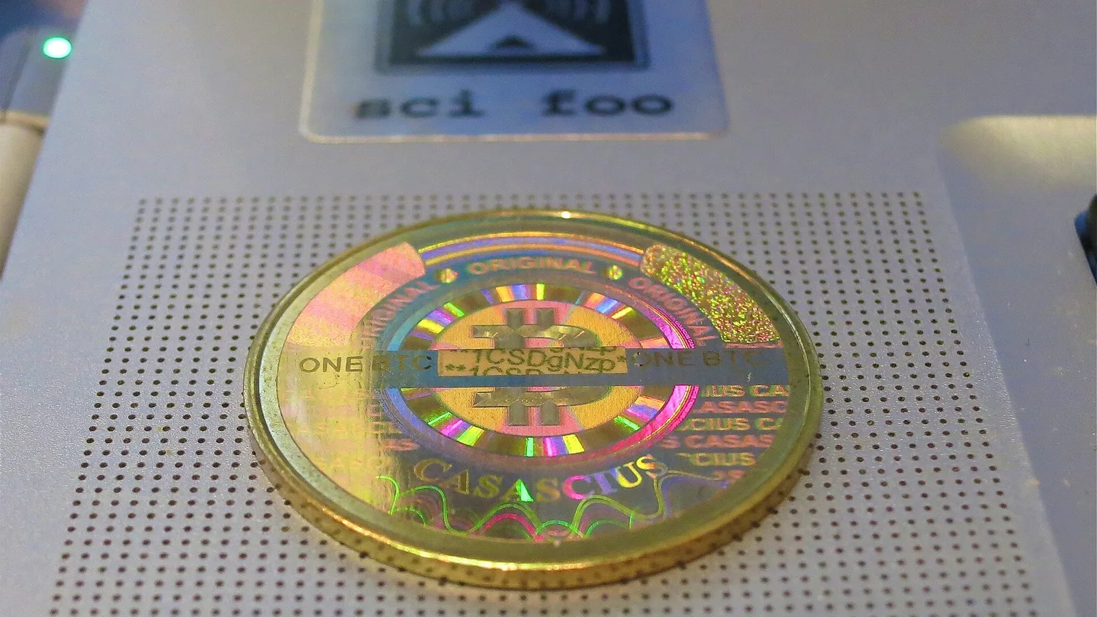 Moeda física de Bitcoin do modelo Casascius, com holograma dourado, sobre um equipamento