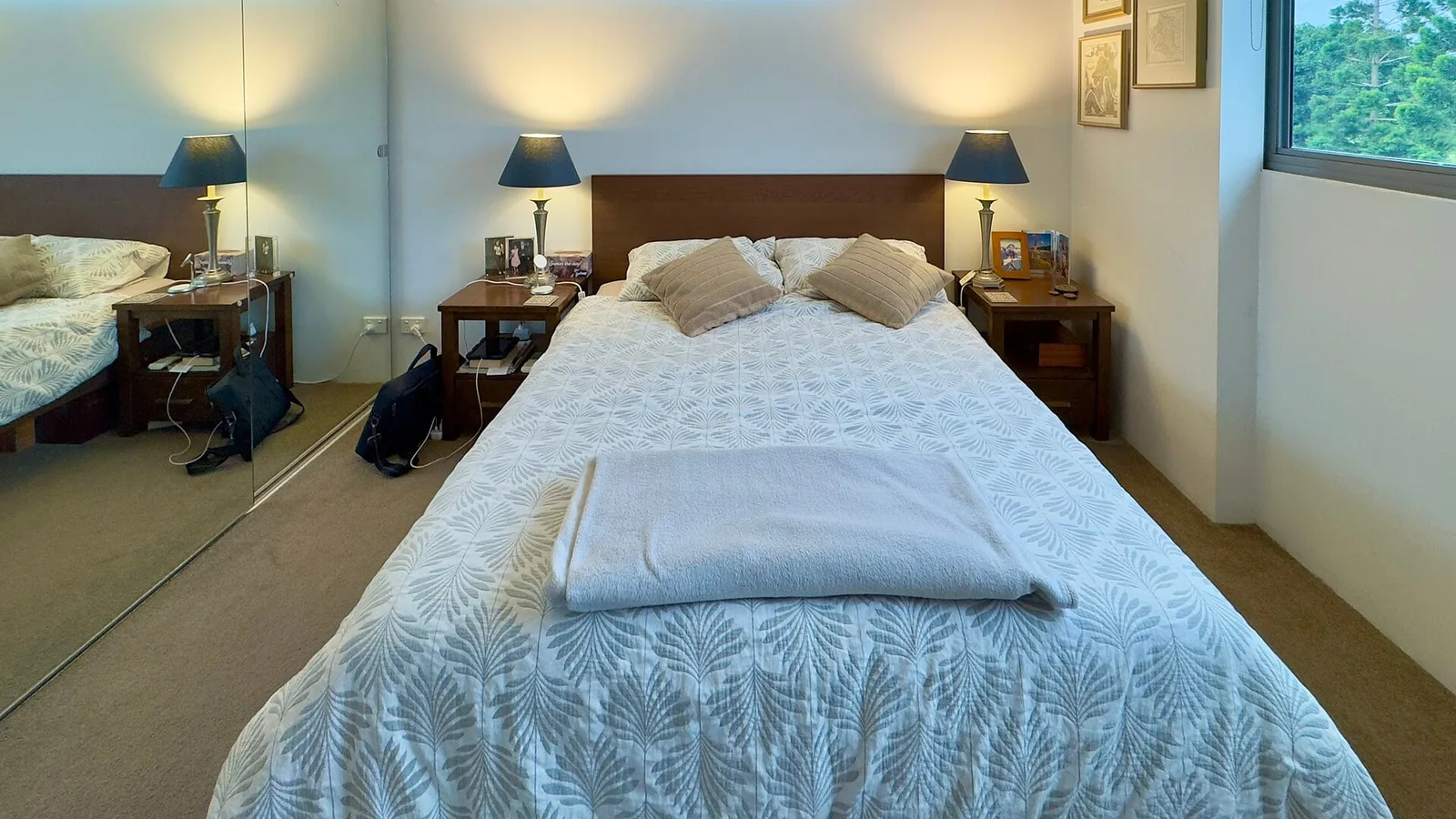 Quarto com cama de casal arrumada, duas luminárias de cabeceira acesas e persianas fechadas