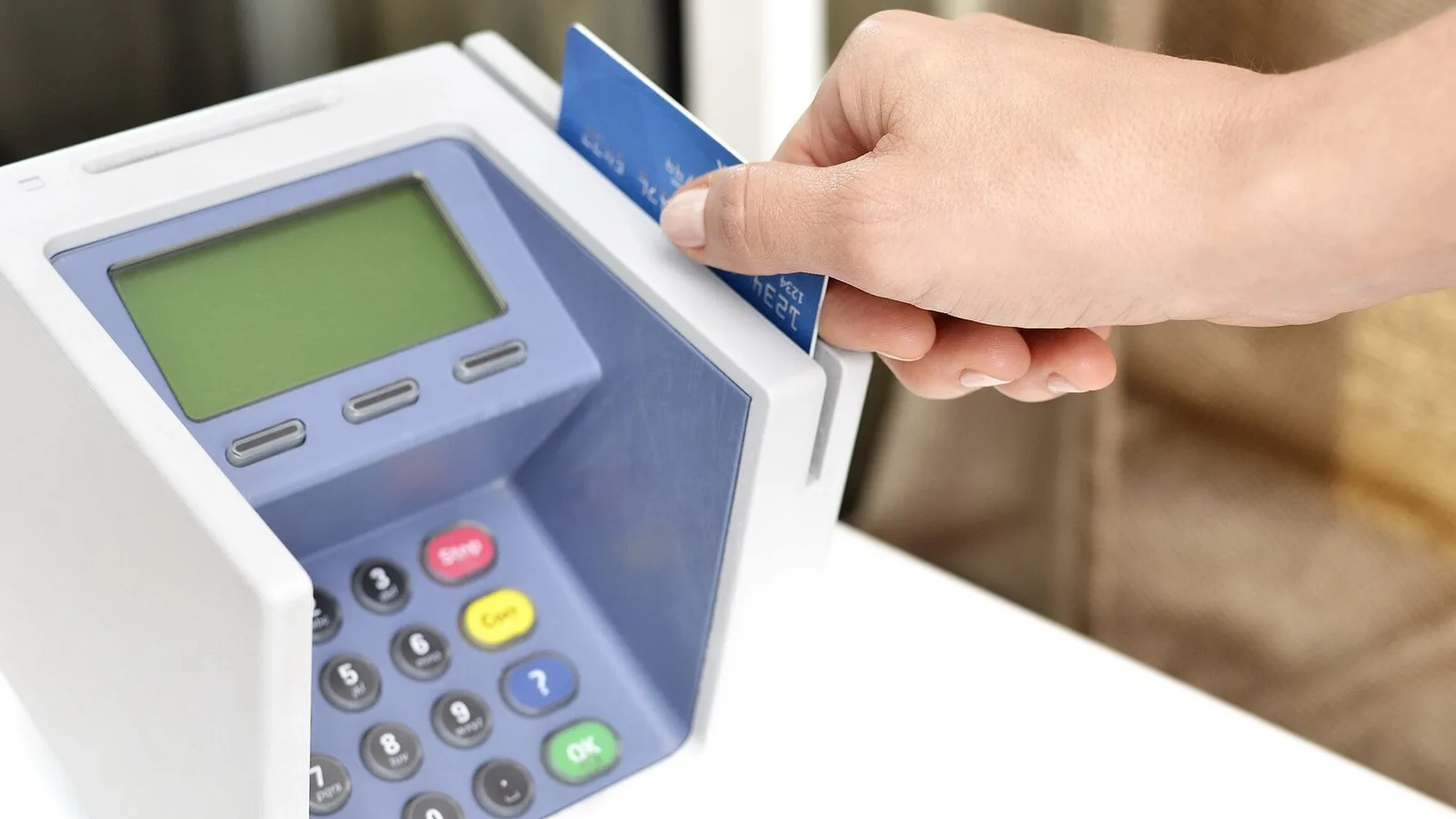 Mão inserindo um cartão azul em uma maquininha de pagamento com visor e teclado numérico