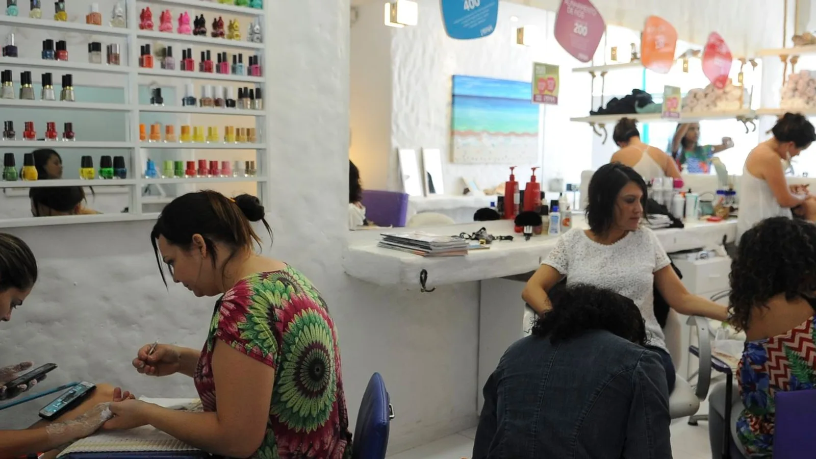Cabeleireiras e manicures atendem clientes em um salão de beleza