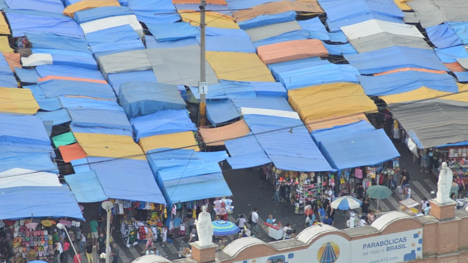 Vista aérea de barracas de comerciantes sob lonas coloridas em feira de rua em Aparecida (SP)
