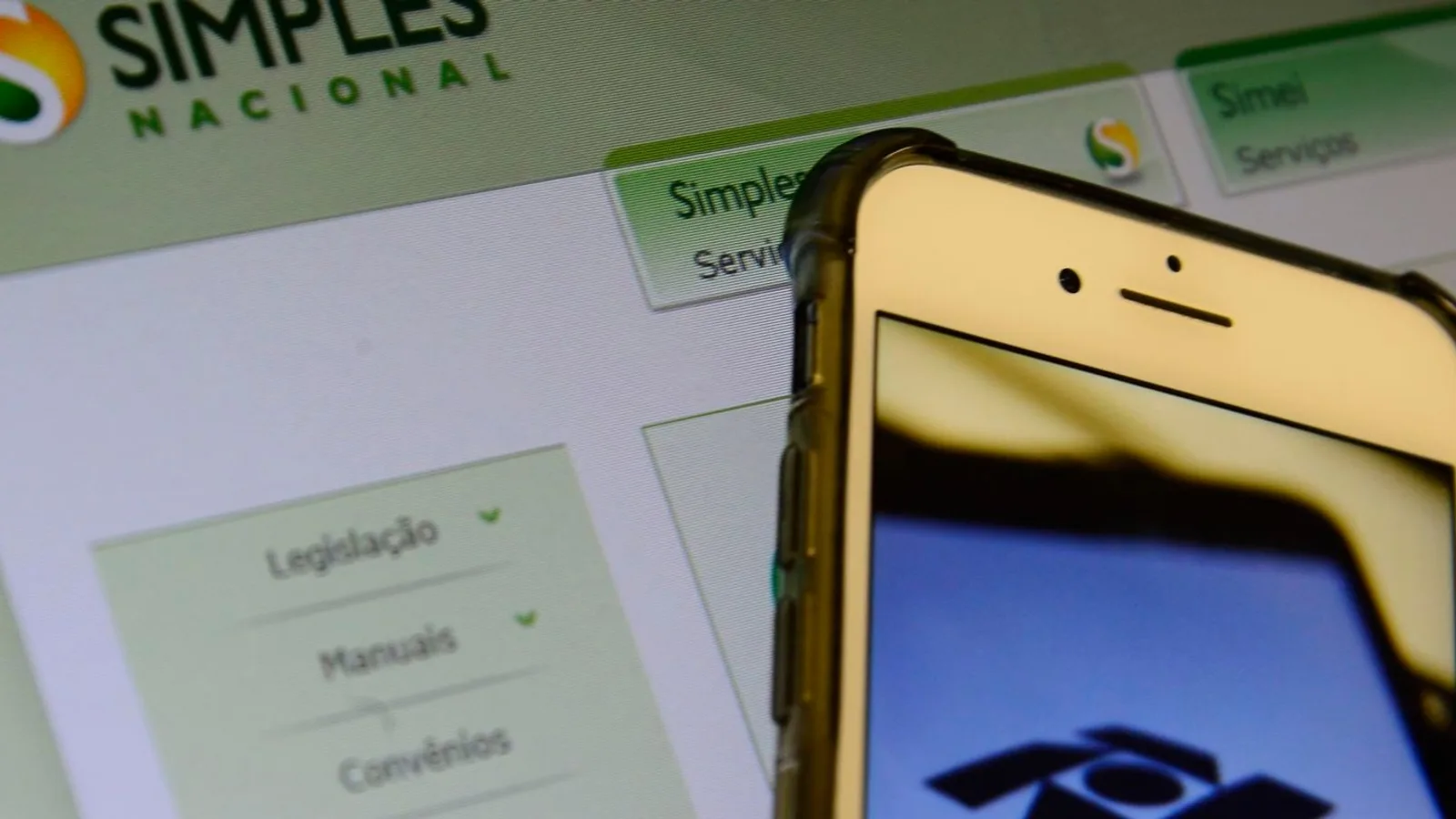 Página do Simples Nacional na tela do computador, ao lado de um celular com o símbolo da Receita Federal