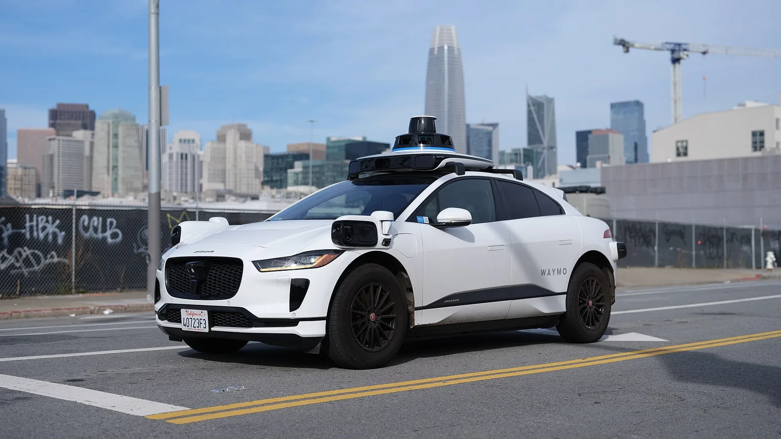 Robotáxi da Waymo, um Jaguar I-Pace branco com sensores no teto, circulando sem motorista em San Francisco