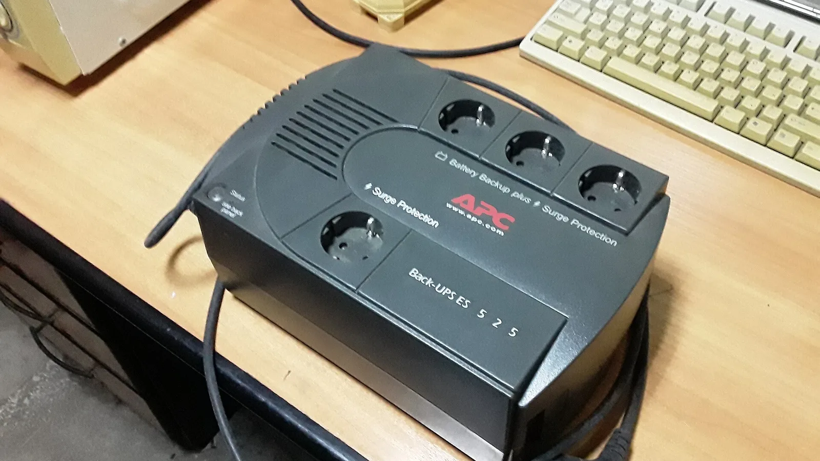 Nobreak APC Back-UPS ES 525 sobre uma mesa, ao lado de um teclado de computador