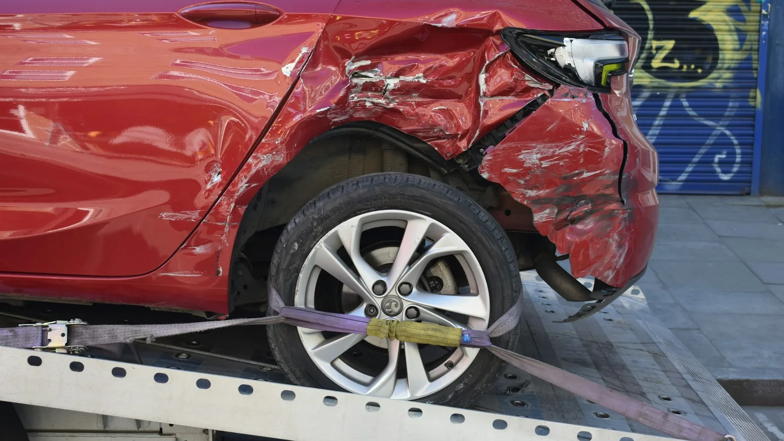 Carro vermelho com a lateral traseira amassada sendo transportado em um guincho
