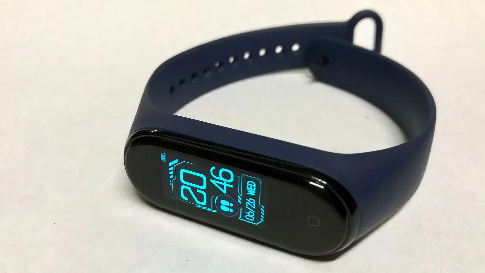 Smartband de pulseira azul com a tela ligada mostrando a hora, em fundo branco