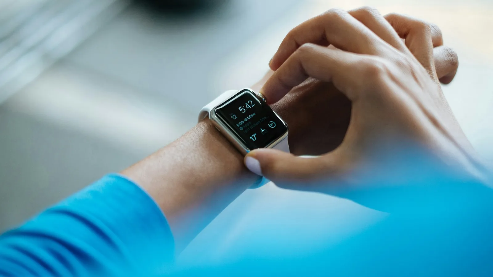 Pessoa de camiseta azul de treino tocando a tela de um smartwatch no pulso