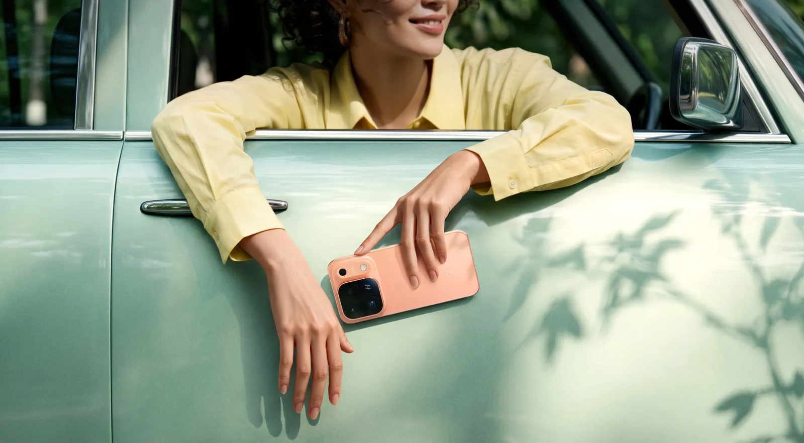 Mão segurando o Find X10 Pro Max laranja apoiada na porta de um carro verde-claro